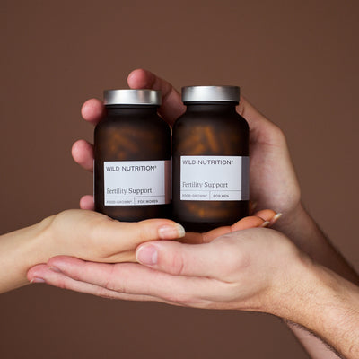 Male and female hand holding fertility support duo supplements - Wild Nutrition