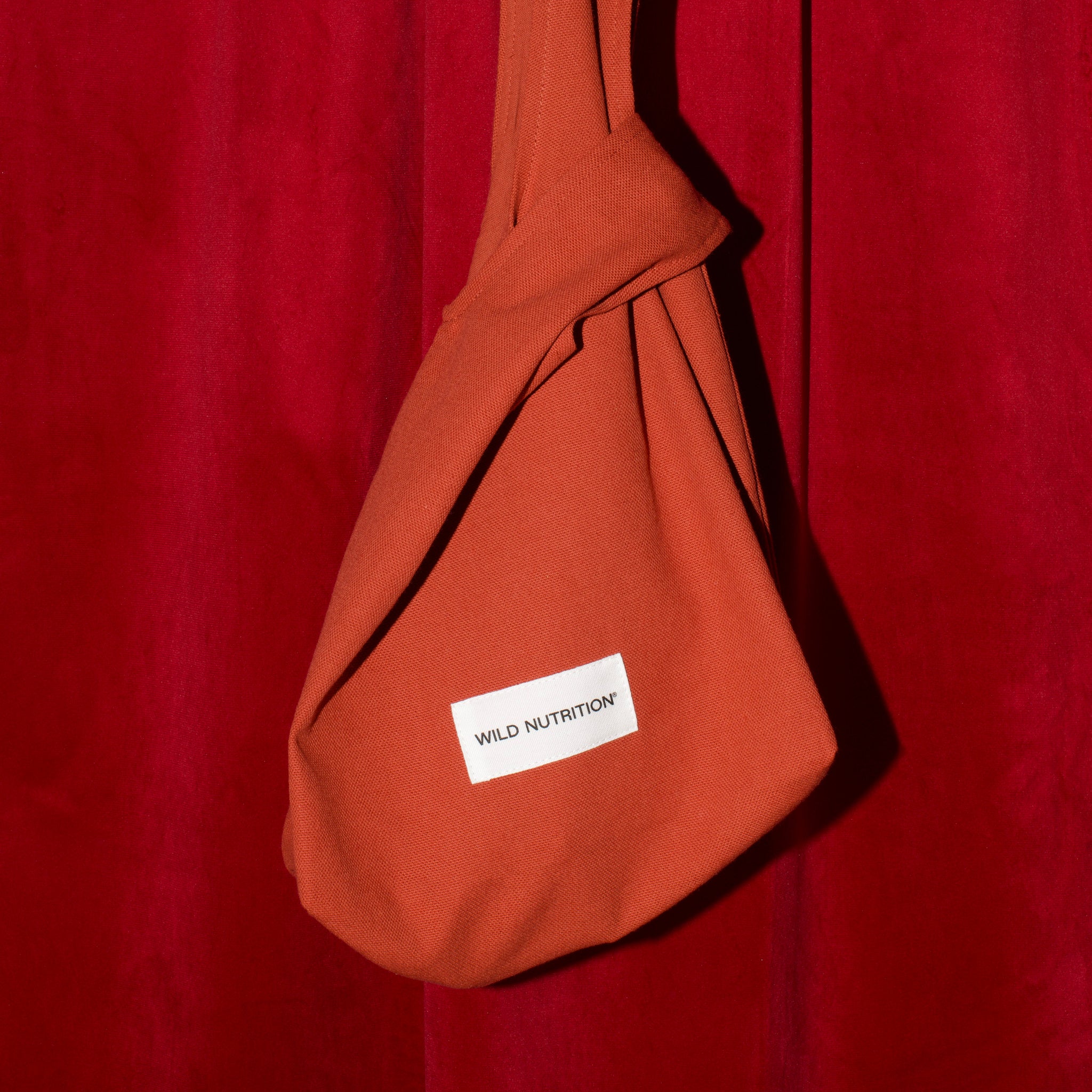 Burnt orange sling bag with a white label on a red background