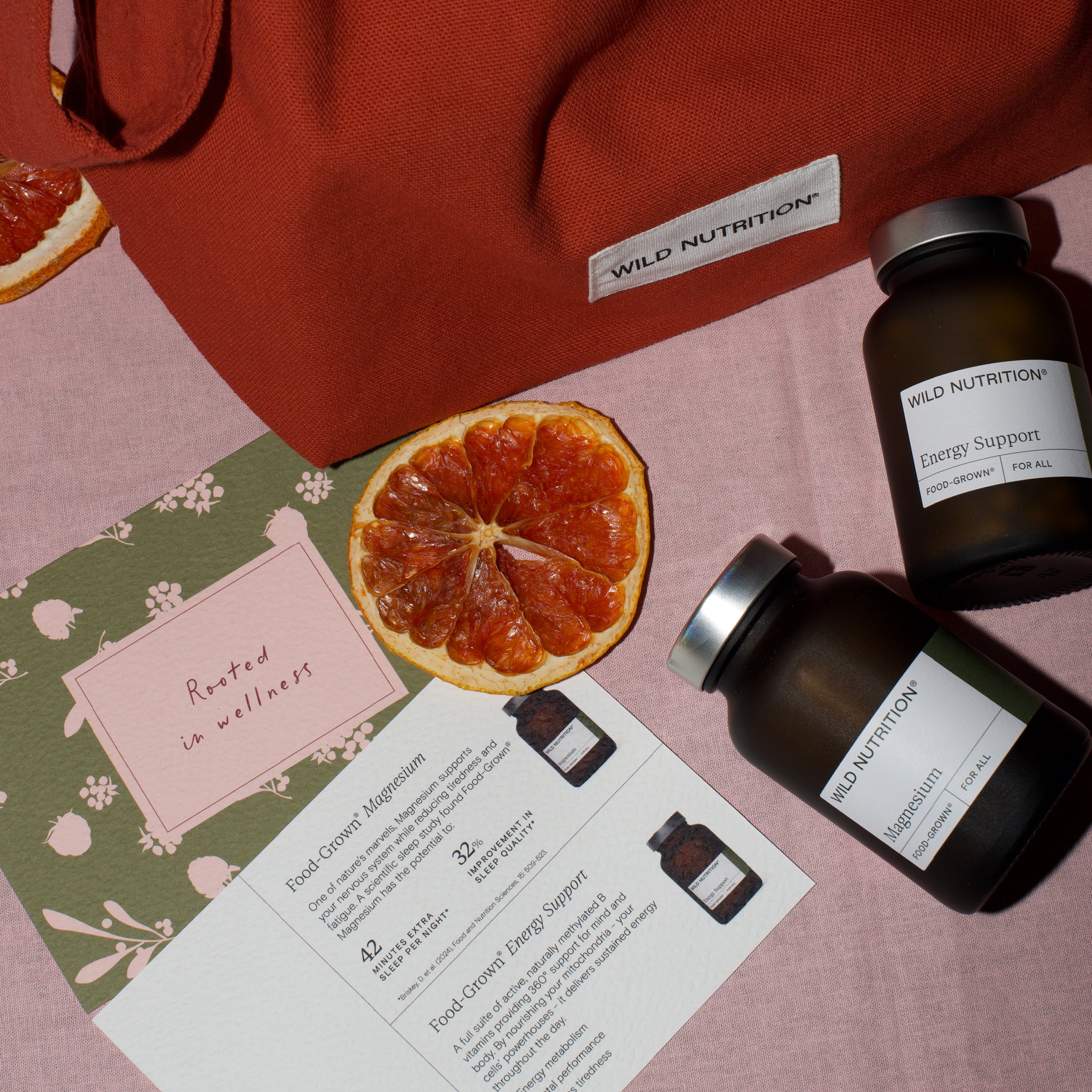 Two bottles of Wild Nutrition supplements on a pink surface with an orange slice and informational leaflet.