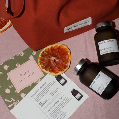 Two bottles of Wild Nutrition supplements on a pink surface with an orange slice and informational leaflet.