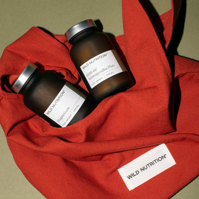Two bottles of Wild Nutrition supplements, Magnesium and Ashwagandha on a red fabric bag background
