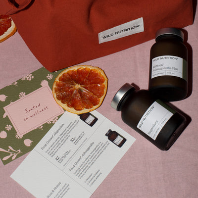 Wild Nutrition supplement bottles of magnesium and ashwagandha with a half-sliced orange and informational card on a pink background