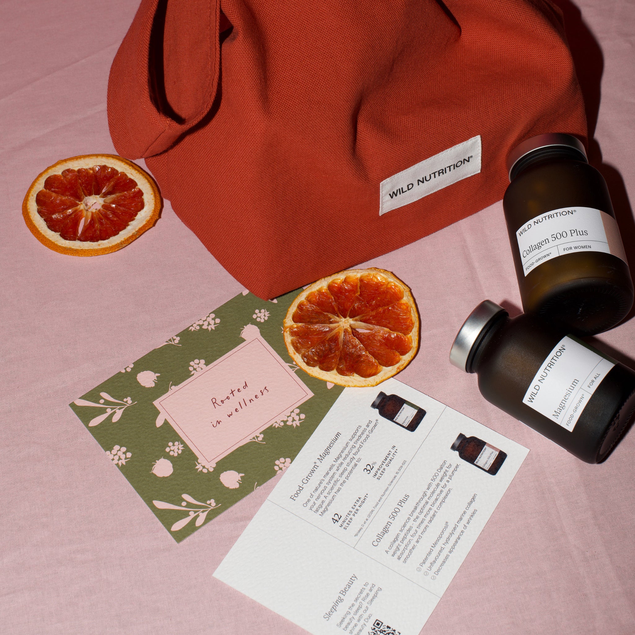 Two bottles of Wild Nutrition supplements, collagen and magnesium on a pink surface with dried oranges and a card.