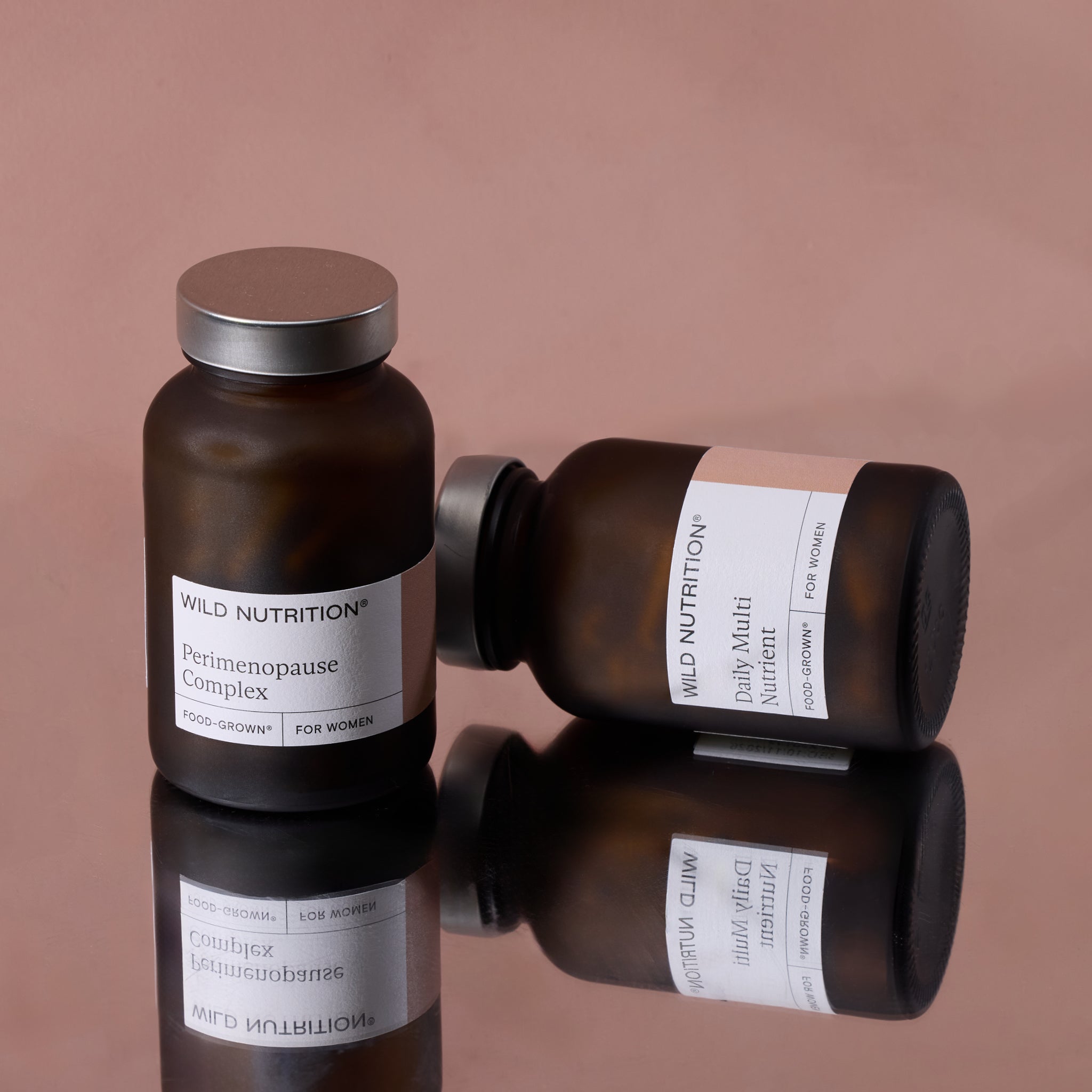 Wild Nutrition Perimenopause Complex and Daily Multi Nutrient supplements for women displayed on pink reflective surface