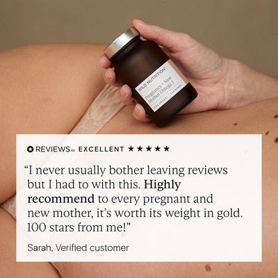 Hand holding a jar with a customer review overlay on a beige background. Review is for wild nutrition pregnancy omega 3 supplement.