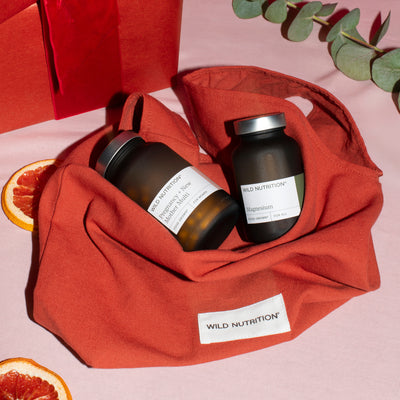 Two jars of Wild Nutrition supplements on a branded red bag with a pink background