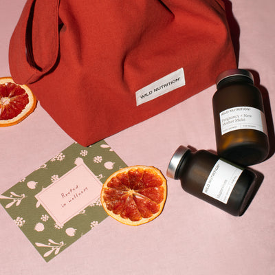 Two jars of Wild Nutrition supplements on a pink surface with blood oranges and a red bag.