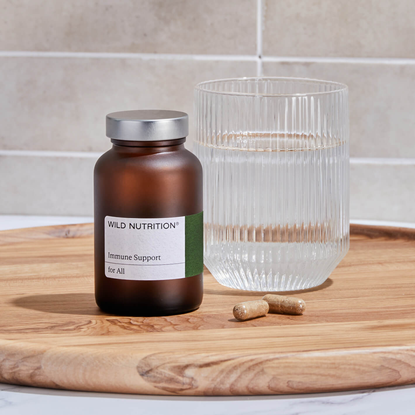 Wild Nutrition Immune Support Duo bottle with two capsules and a glass of water on a wooden tray.