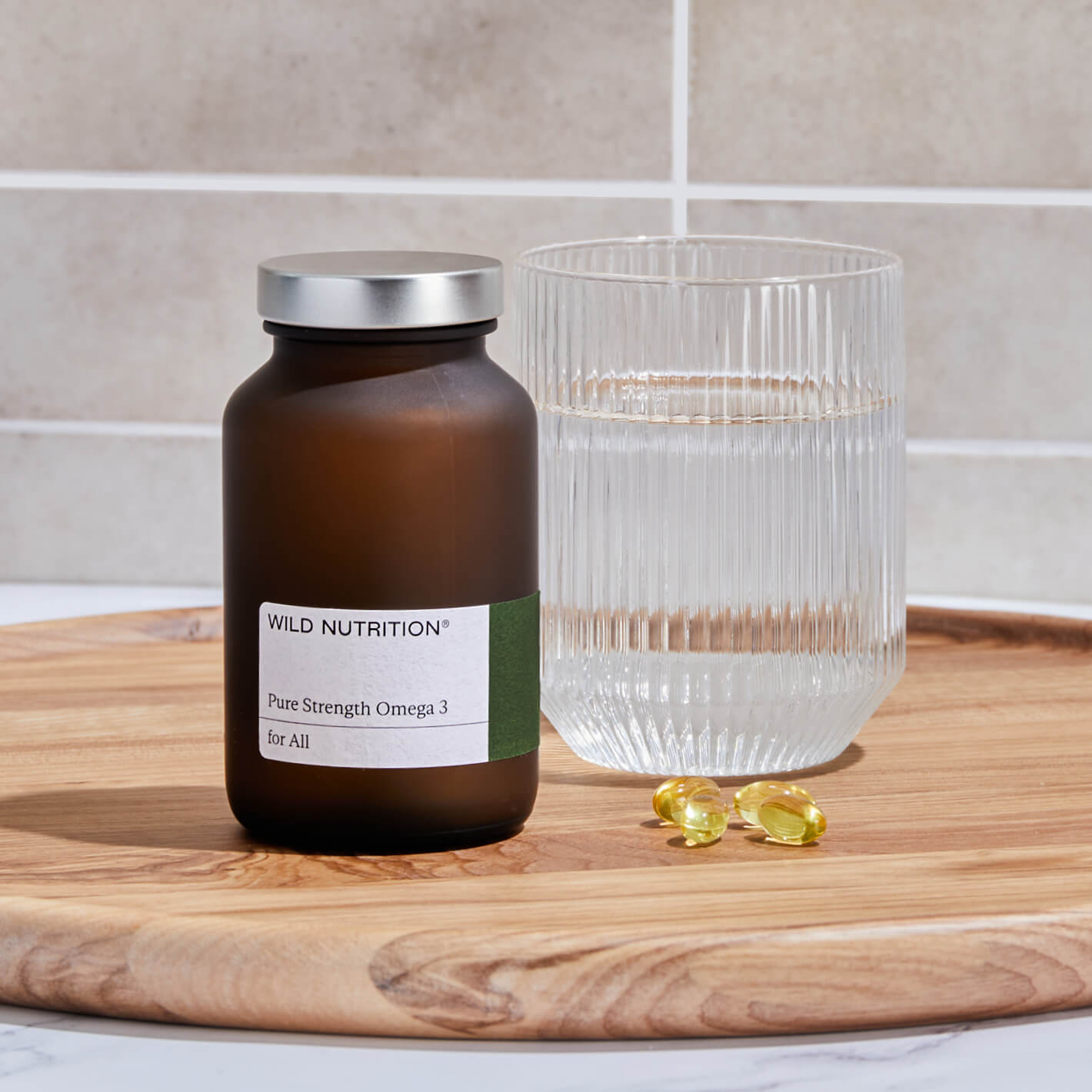 Wild Nutrition Pure Strength Omega 3 bottle, a glass of water, and omega-3 capsules on a wooden tray.