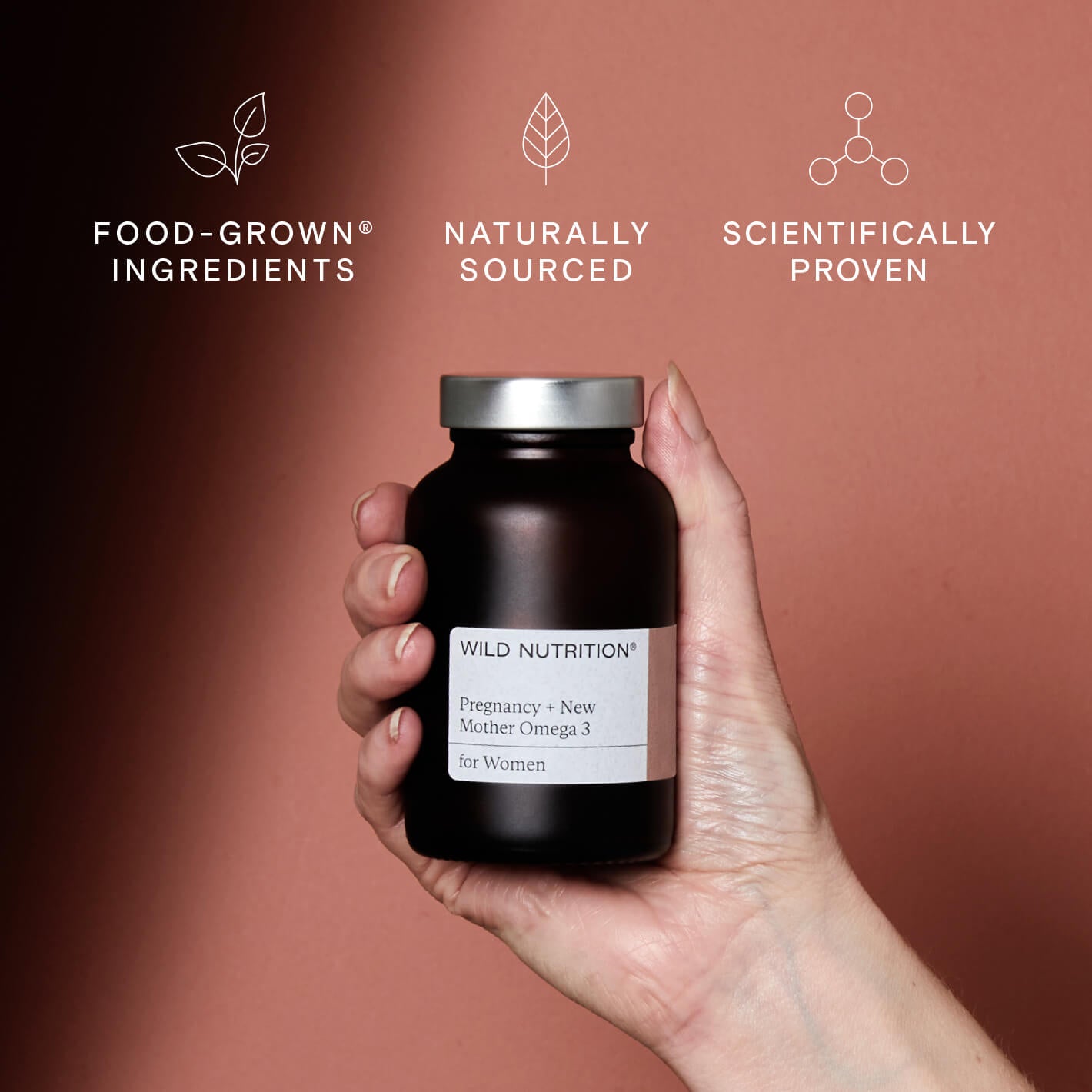 Hand holding Wild Nutrition® Pregnancy + New Mother Omega 3 supplement, highlighting food-grown ingredients.