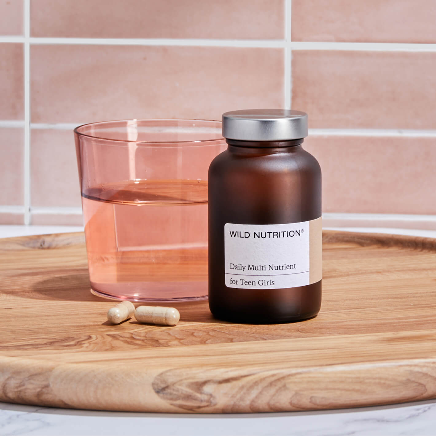 Wild Nutrition Daily Multi Nutrient for Teen Girls with a glass of water and capsules on a wooden tray.